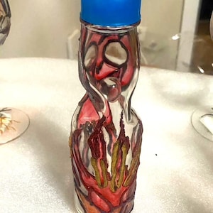 May include: A clear glass bottle with a blue cap. The bottle is decorated with red, orange, and gold abstract designs. The bottle's shape is unique, with a rounded base and a narrow neck. The bottle is likely for beverages.