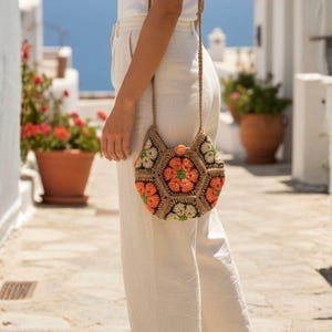 Può includere: Borsa a tracolla esagonale all'uncinetto con un design floreale arancione, verde e beige. La borsa ha una tracolla lunga e sottile. La borsa è in stile bohémien.