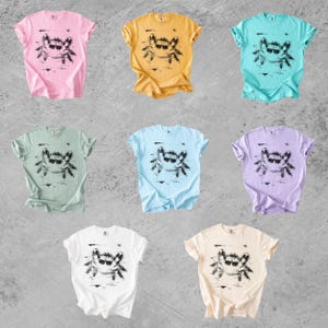 Puede incluir: Ocho camisetas de manga corta y cuello redondo en varios colores pastel y s&oacute;lidos, incluyendo rosa, amarillo, turquesa, verde claro, azul claro, lavanda, blanco y crema. Cada camiseta presenta un estampado gr&aacute;fico negro de un cangrejo con gafas.