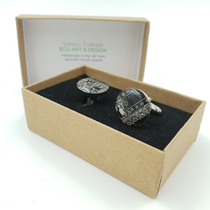 May include: A pair of silver cufflinks with black and white circuit board designs. The cufflinks are in a brown box with the text "Sarah Turner Eco Art & Design Handmade in the UK from recycled circuit boards".