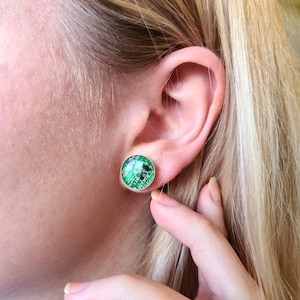 May include: A pair of green and black circuit board earrings. The earrings are round and have a silver backing.