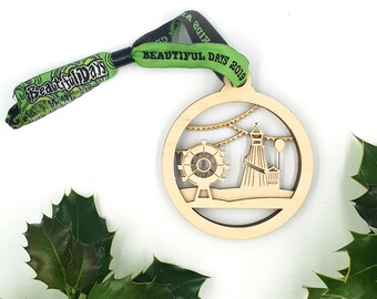 May include: A wooden ornament shaped like a circle with a cut-out design of a Ferris wheel and a tower. The ornament is attached to a green and black wristband with the text "Beautiful Days 2019".