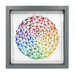 May include: A framed artwork featuring a circular arrangement of colorful dragonfly cutouts. The dragonflies are arranged in a gradient of colors, from red to purple to blue to green to yellow. The frame is gray.