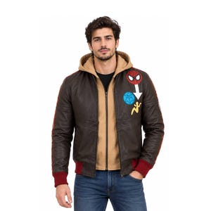 May include: A dark brown leather bomber jacket with a tan hooded lining, red ribbed cuffs, and a front zipper. The chest features embroidered patches including a Spider-Man mask, a blue spiderweb circle, a white arrow, and a yellow silhouette figure.