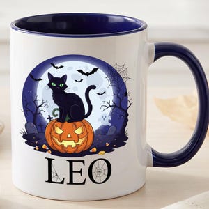 May include: A white ceramic mug with a dark blue interior and handle. The front features a graphic of a black cat sitting on a glowing orange jack-o'-lantern against a full moon, bats, and trees. The name LEO is printed in black below the graphic.