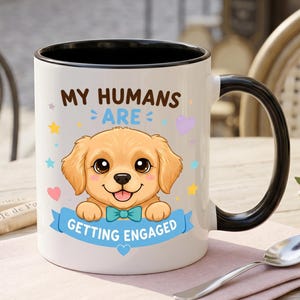 Puede incluir: Una taza de cerámica blanca con interior y asa negros, que presenta un cachorro dorado de dibujos animados con una pajarita color cerceta. El texto MY HUMANS ARE GETTING ENGAGED está rodeado de estrellas y corazones coloridos.