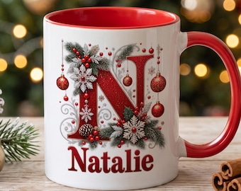 Könnte beinhalten: Ein weißer Keramikbecher mit rotem Innenraum und Henkel, verziert mit einem großen roten Buchstaben N, Tannenzweigen, Schneeflocken, roten Kugeln und Beeren. Der Name Natalie ist in roter Schrift unter dem Buchstaben N aufgedruckt.