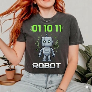 Puede incluir: Camiseta gris oscuro con un diseño de robot. El diseño incluye el código binario "01 10 11" en verde encima del robot y la palabra "ROBOT" en blanco debajo. El robot es gris con detalles verdes de placa de circuito.
