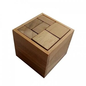 May include: A wooden puzzle cube with several rectangular pieces partially filling the top opening. The cube and puzzle pieces are made of light brown wood. The puzzle is designed to fit the pieces into the cube.
