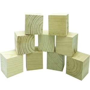 May include: A collection of ten unfinished wooden blocks, each a perfect cube. The natural wood grain is visible on the sides of the blocks, with some showing circular growth rings. The blocks are arranged in a pyramid shape against a white background.