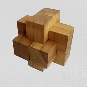 Könnte beinhalten: Ein Holzpuzzle aus ineinandergreifenden Blöcken. Die Blöcke sind hellbraun und in einer dreidimensionalen Form angeordnet. Das Puzzle ist so konzipiert, dass es durch Manipulation der Blöcke gelöst werden kann.
