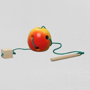 May include: A wooden toy featuring a red and yellow ball with holes, connected by green string to a small wooden cube and a wooden stick. The ball has a smooth, glossy finish.