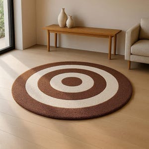 Könnte beinhalten: Ein runder, brauner Teppich mit einem Design aus cremefarbenen konzentrischen Kreisen. Der Teppich liegt auf einem hellen Holzboden. Der Teppich ist ein dekoratives Element für ein Wohn- oder Schlafzimmer.