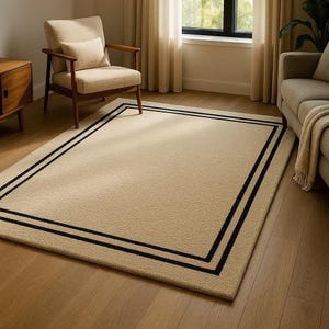 Puede incluir: Alfombra rectangular beige con un borde doble negro. Está colocada sobre un suelo de madera. La habitación incluye una silla, un sofá y una ventana con cortinas, creando un ambiente acogedor.