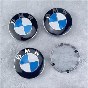 Op de afbeelding: Vier zwarte, blauwe en witte BMW wieldopjes. Drie doppen hebben het BMW-logo met de letters "BMW" in wit. Eén dop is omgedraaid en toont de achterkant.