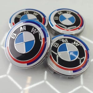 May include: Four BMW wheel center caps. Each cap features the BMW logo in the center, a blue and white emblem, surrounded by a black ring, and a red, white, and blue outer ring. The caps have a silver base and are designed for automotive use.