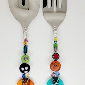 May include: A set of two silver serving utensils with colorful glass beads and wire wrapped handles. The utensils are a spoon and a fork.
