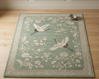 May include: A rectangular area rug in a soft sage green hue featuring a cream-coloured Greek key border. The central design displays two white cranes in flight surrounded by delicate cream-coloured floral branches and blossoms.
