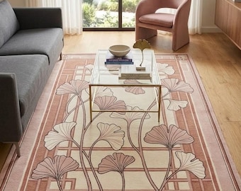 May include: A rectangular area rug featuring a cream-coloured centre with a geometric border in shades of dusty rose and terracotta. The rug is decorated with a repeating pattern of stylised ginkgo leaves on long, slender stems in dark brown outlines.