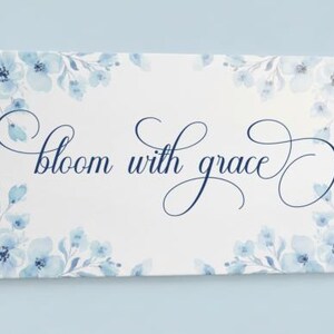 May include: A rectangular canvas print with the words "bloom with grace" in elegant script. The print is decorated with watercolor-style blue floral accents around the edges, set against a white background.