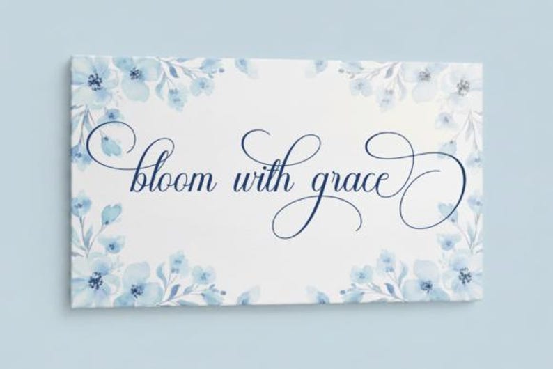 May include: A rectangular canvas print with the words "bloom with grace" in elegant script. The print is decorated with watercolor-style blue floral accents around the edges, set against a white background.