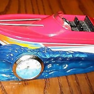 May include: A red and white speedboat figurine with a blue wave base. The boat has a black and white striped interior and a gold-colored clock face.