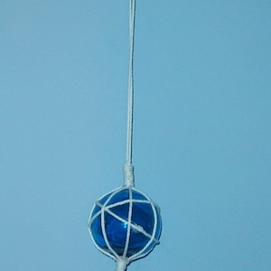 May include: A blue glass fishing float with a white rope net and a white tassel hanging from a white ceiling hook.