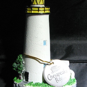 May include: White lighthouse figurine with a yellow and black striped roof. The base of the figurine is green and has the text "Chesapeake Bay" and "Ocracoke, NC" on it.