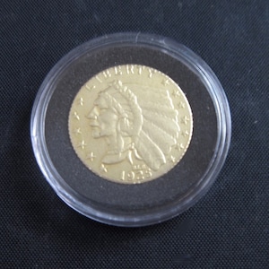 Op de afbeelding: Een gouden munt met de inscriptie "LIBERTY" en het jaar "1925" op de voorkant. De munt toont het profiel van een indiaanse man met een hoofdtooi.