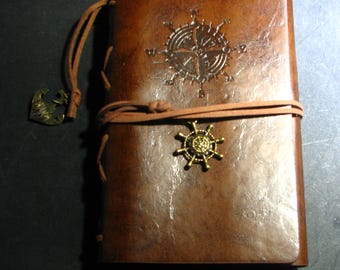 May include: A brown leather journal with a compass and anchor design. The journal has a leather strap closure and a metal compass charm.