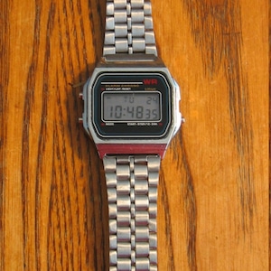 Puede incluir: Un reloj de pulsera digital plateado con una esfera rectangular y una correa de metal. El reloj muestra la hora 10:48:35. El reloj tiene el texto "WR" y "ALARM CHRONO" en la esfera.