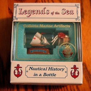 Puede incluir: Una caja blanca con un borde azul y verde, que presenta un barco en miniatura en una botella. La caja dice "Legends of the Sea" y "Collecta Marine Artifacts". El barco es un "Revenue Cutter" y la caja también dice "Nautical History in a Bottle".