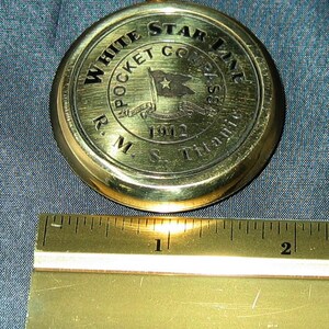 Puede incluir: Una br&uacute;jula de bolsillo de lat&oacute;n con un logotipo de White Star Line y el texto "R.M.S. Titanic 1912".
