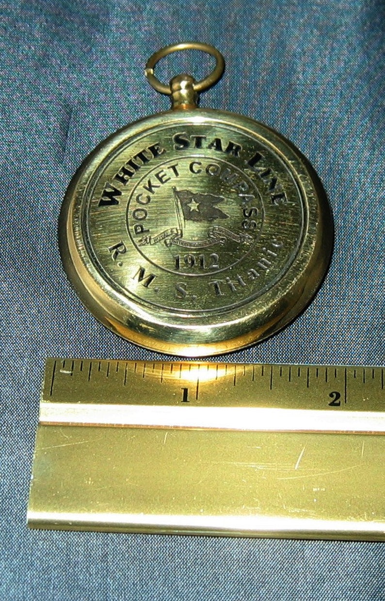 Puede incluir: Una br&uacute;jula de bolsillo de lat&oacute;n con un logotipo de White Star Line y el texto "R.M.S. Titanic 1912".