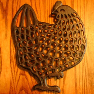 May include: A cast iron chicken-shaped hot pad with a decorative, openwork design. The hot pad is dark brown and has a rustic look.