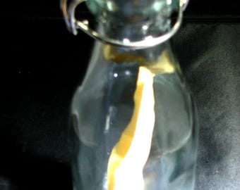 May include: A clear glass bottle with a white lid and a metal closure. The bottle is filled with a light yellow liquid.