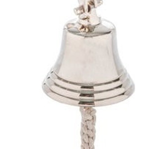 Könnte beinhalten: Eine polierte silberne Schiffsglocke mit einem Seilzug. Die Glocke ist an einer Wandhalterung mit einem gebogenen Arm befestigt.