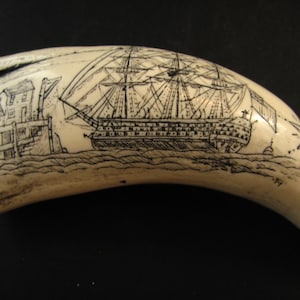 May include: A carved ivory tusk with a detailed engraving of a tall ship sailing near a coastal town. The artwork is rendered in black ink, showcasing the ship's masts, sails, and the architectural details of the buildings. The tusk has a curved shape.