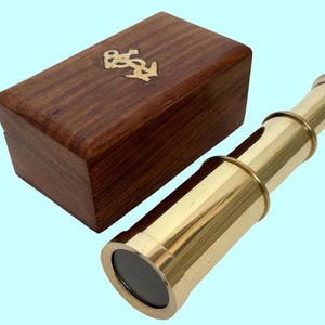 Peut inclure: Une lunette de marine en laiton avec une boîte en bois. La boîte a un motif d'ancre sur le dessus.