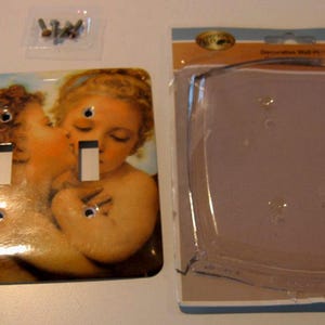 May include: Decorative light switch cover featuring a Renaissance-style painting of two cherubs. The cover has two switch openings and includes mounting screws. A clear plastic wall plate is also included.