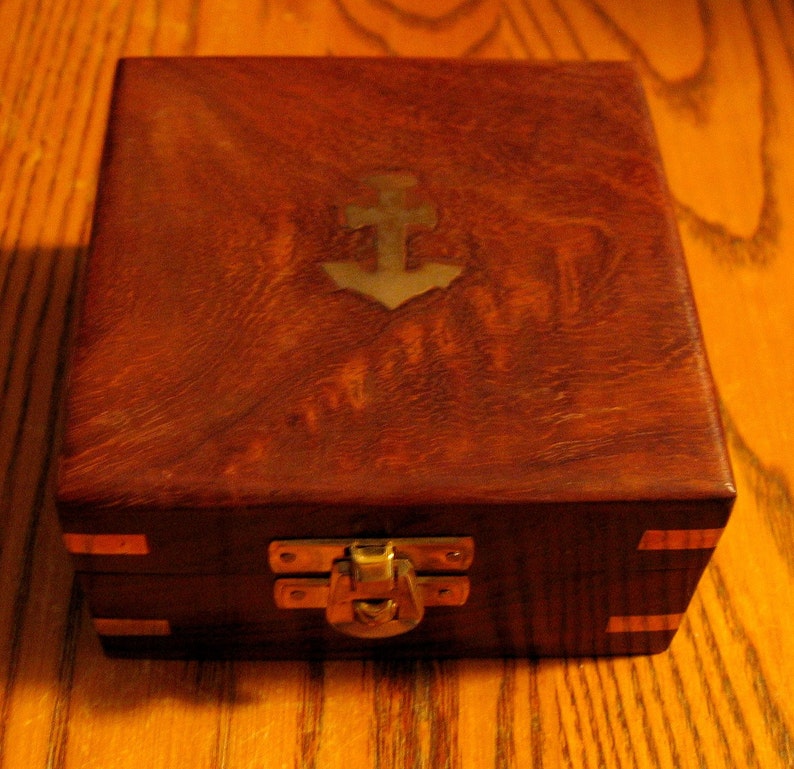 Puede incluir: Una caja de madera con un dise&ntilde;o de ancla de lat&oacute;n en la tapa. La caja tiene un pestillo y bisagras de lat&oacute;n.