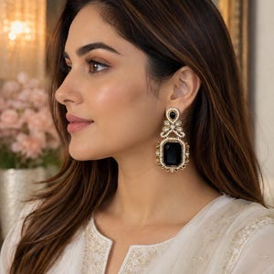 May include: A pair of statement earrings featuring a large rectangular black center stone surrounded by a border of small white pearls and gold-toned metal filigree. The top section includes a smaller black stone and pearl accents.
