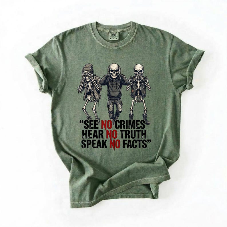 May include: Green t-shirt featuring a graphic of three skeletons in various poses, with one covering its eyes, one its ears, and one its mouth. The text "SEE NO CRIMES HEAR NO TRUTH SPEAK NO FACTS" is below the skeletons.