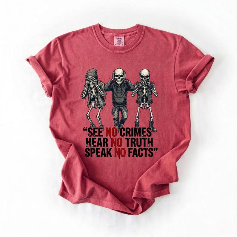 May include: A red t-shirt featuring a graphic of three skeletons in the 'see no evil, hear no evil, speak no evil' pose. The text on the shirt reads: "SEE NO CRIMES, HEAR NO TRUTH, SPEAK NO FACTS."