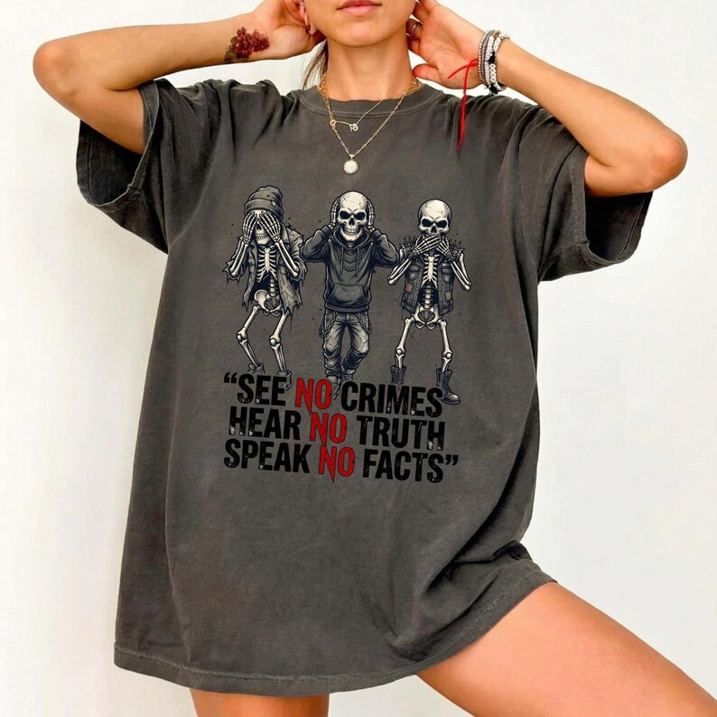 May include: Dark gray t-shirt featuring a graphic of three skeletons in the 'see no evil, hear no evil, speak no evil' pose. The text below reads "SEE NO CRIMES, HEAR NO TRUTH, SPEAK NO FACTS".