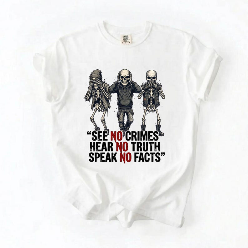 May include: White t-shirt featuring a graphic of three skeletons in the 'see no evil, hear no evil, speak no evil' pose. The skeletons are wearing a beanie, hoodie, and vest. Below the skeletons is the text: "SEE NO CRIMES HEAR NO TRUTH SPEAK NO FACTS".
