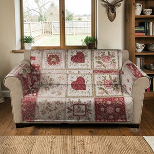 Peut inclure: Un canapé beige recouvert d'une housse à motifs floraux et en forme de cœur. La housse présente un motif patchwork avec des roses rouges et roses, des cœurs et des carrés floraux. Le canapé est devant une fenêtre.
