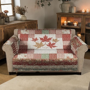 Könnte beinhalten: Beiges Sofa mit einer gesteppten Decke im Patchwork-Design in Rot, Weiß und Grün. Die Decke hat ein zentrales Feld mit gestickten Ahornblättern in Rot- und Goldtönen, was ein gemütliches Herbstthema schafft.