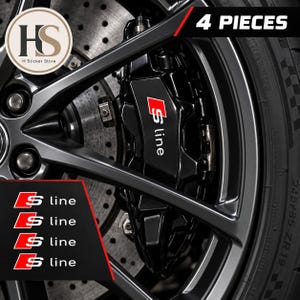 Op de afbeelding: Een set van 4 S line stickers voor remklauwen van auto's. De stickers zijn zwart met een rood vierkant en witte S line tekst. De afbeelding toont de stickers aangebracht op een zwarte remklauw achter een donkergrijze lichtmetalen velg.