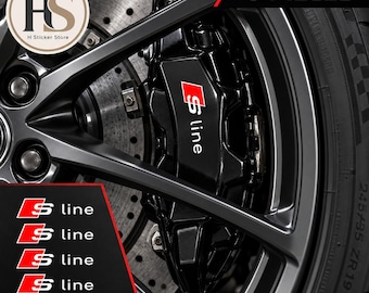 Puede incluir: Un juego de 4 pegatinas S line para pinzas de freno de coche. Las pegatinas son negras con un cuadrado rojo y texto S line en blanco. La imagen muestra las pegatinas aplicadas en una pinza de freno negra tras una llanta gris oscuro.